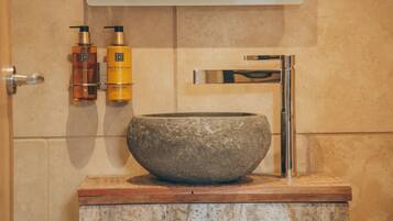 Un baño con un lavabo de piedra, un grifo de cromo y dos botellas de loción en la pared.