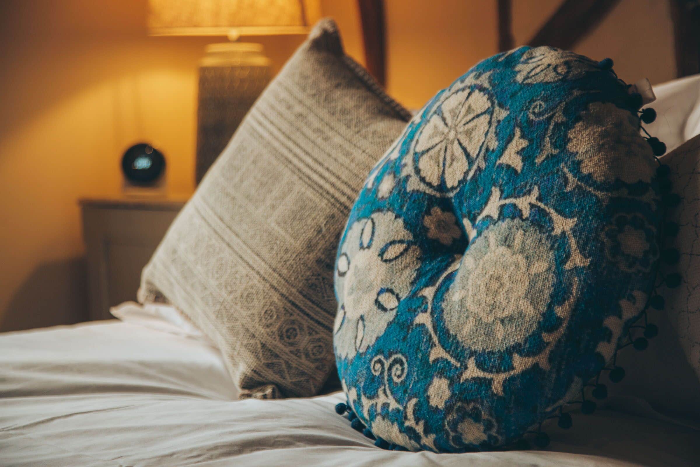 A bed with patterned pillows and a bedside table with a lamp.
