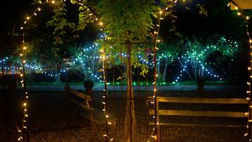 A nighttime outdoor area with string lights, wooden benches, and a tree.