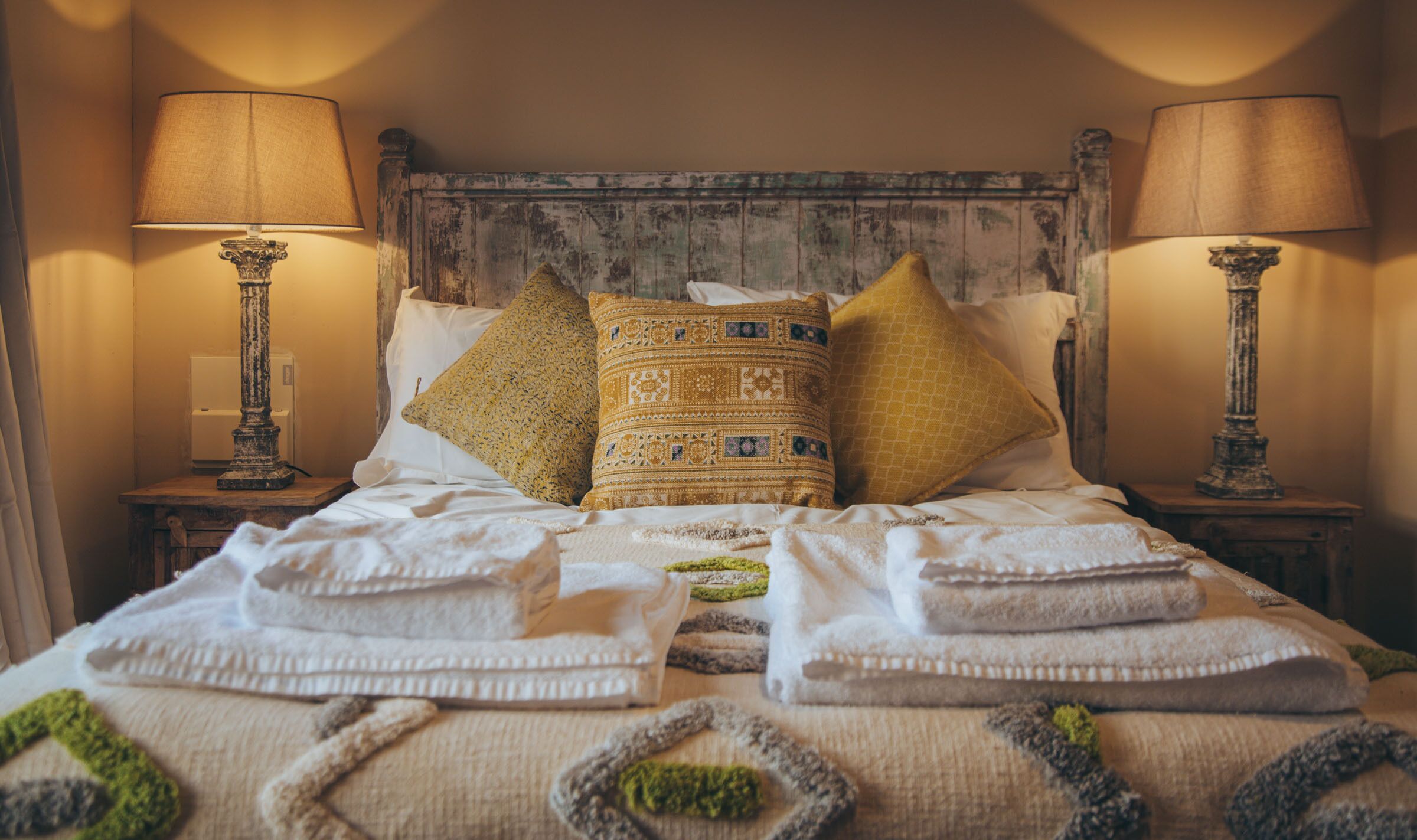 Un lit bien fait, agrémenté de coussins décoratifs, de deux lampes de chevet et d’une tête de lit rustique.