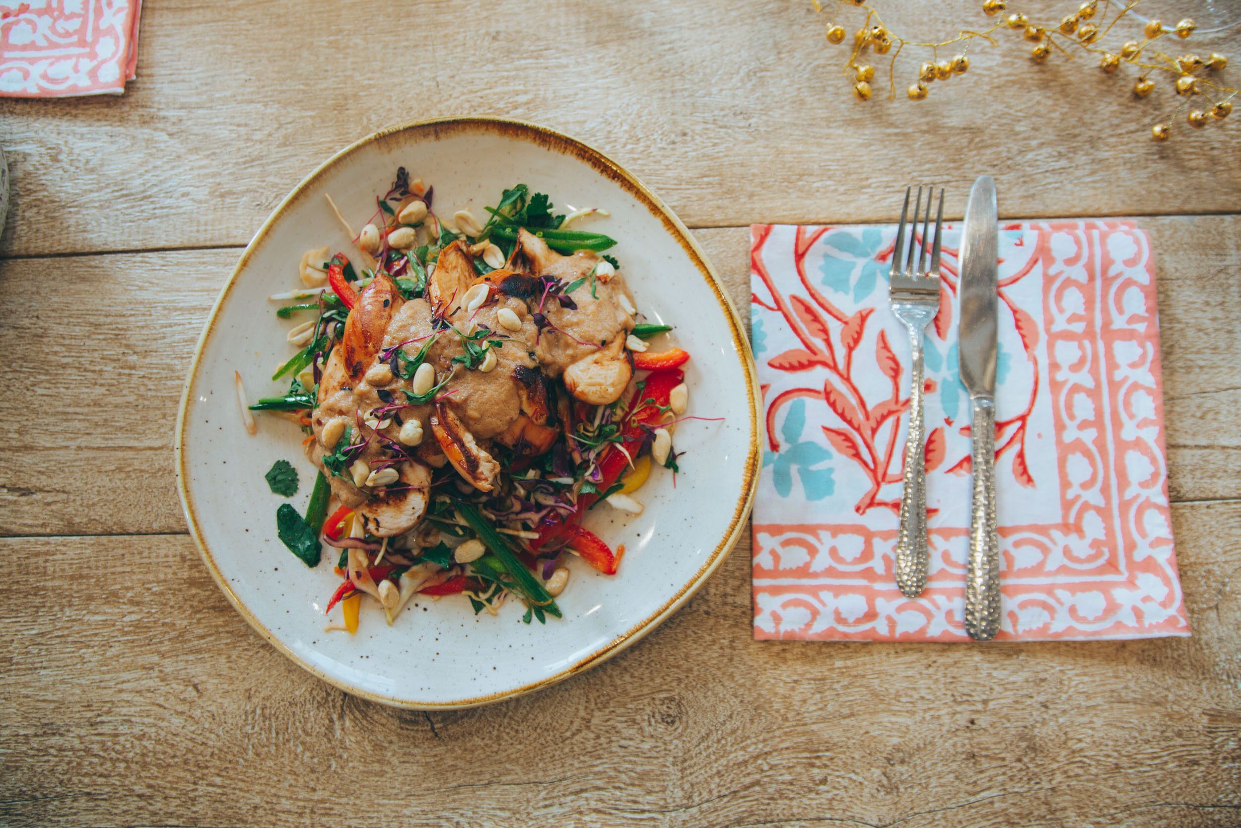 A plate of food on a wooden table with a napkin and cutlery.