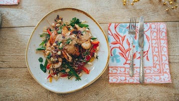 A plate of food on a wooden table with a napkin and cutlery.