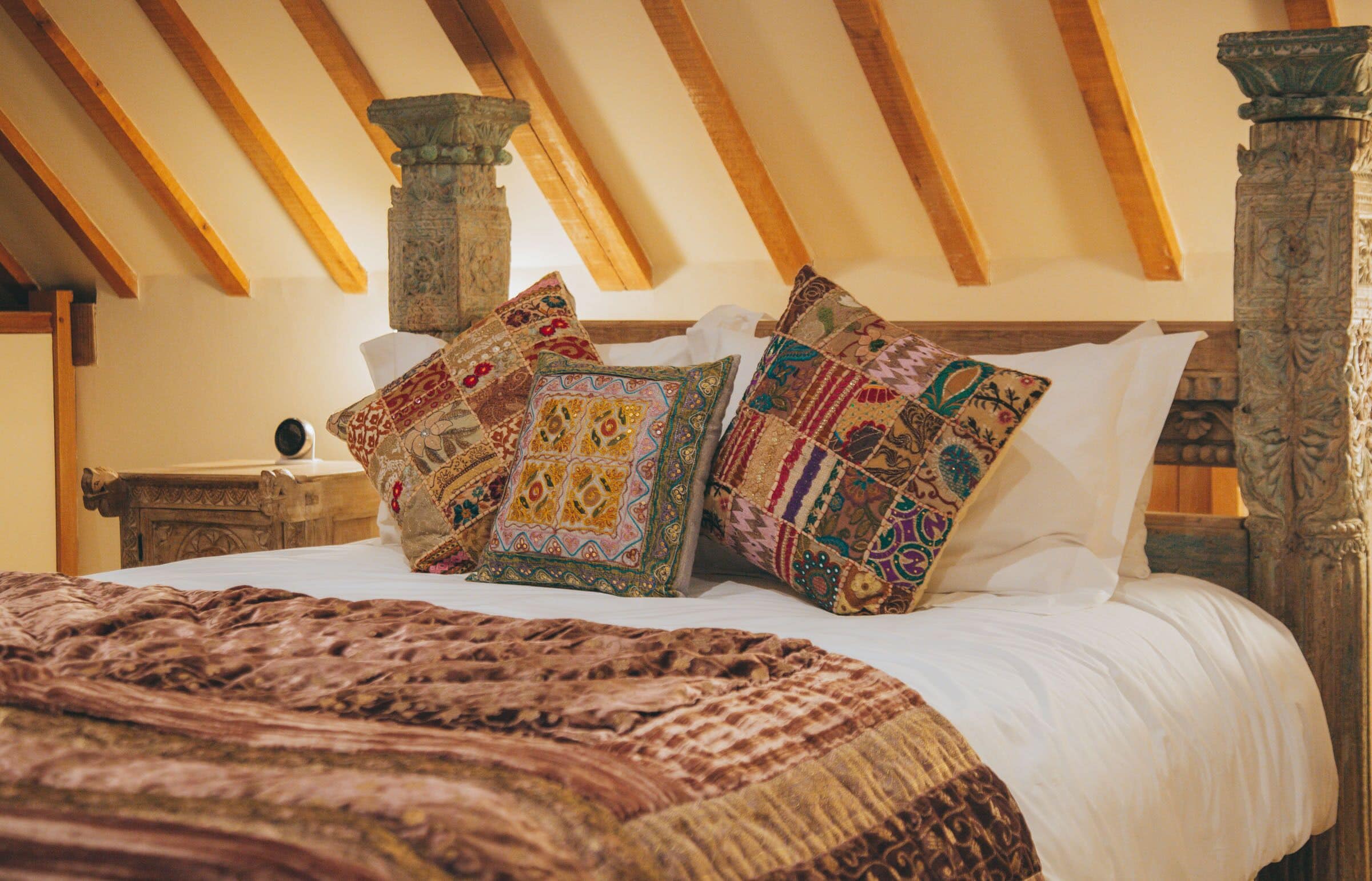A bed with patterned pillows and a brown blanket in a room with wooden beams and stone columns.