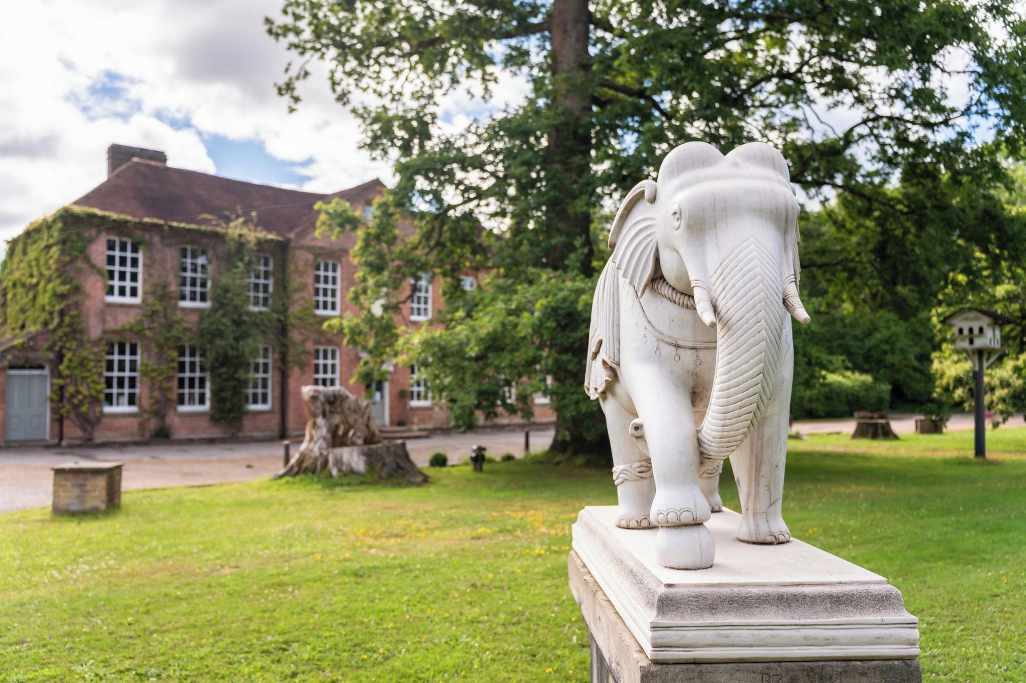 A white elephant statue on a pedestal in a grassy area with a building in the background.