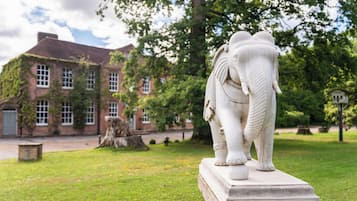 A white elephant statue on a pedestal in a grassy area with a building in the background.