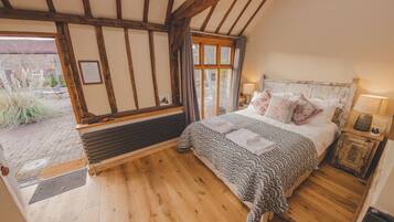 A bedroom with a wooden floor, a bed with patterned bedding, a wooden headboard, and a window with curtains.