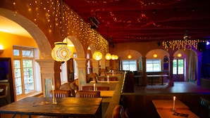 A restaurant with wooden tables and chairs, hanging pendant lights, and a red ceiling. - Trading Boundaries (Uckfield)