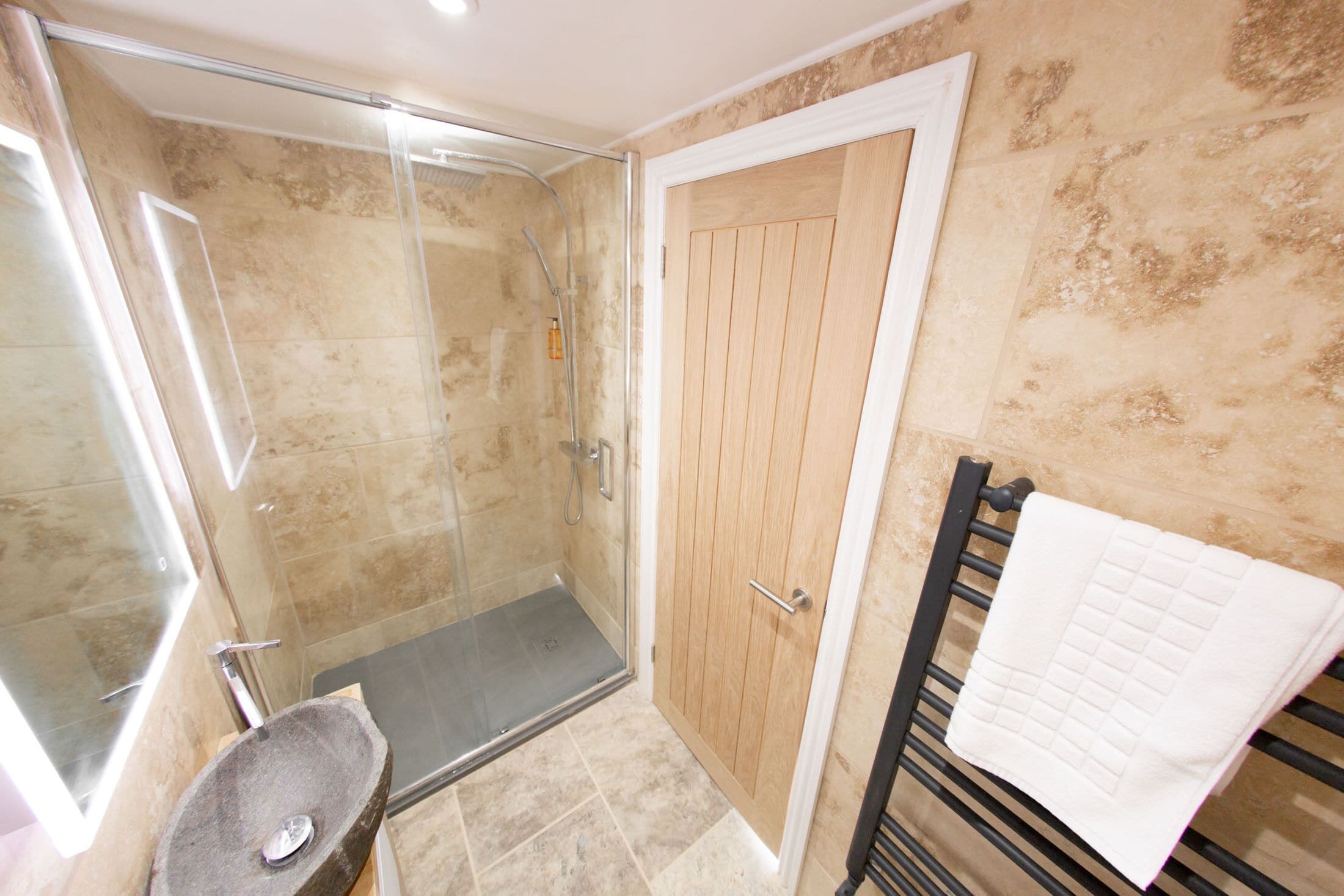 A bathroom with a glass shower enclosure, a wooden door, and a towel rack.