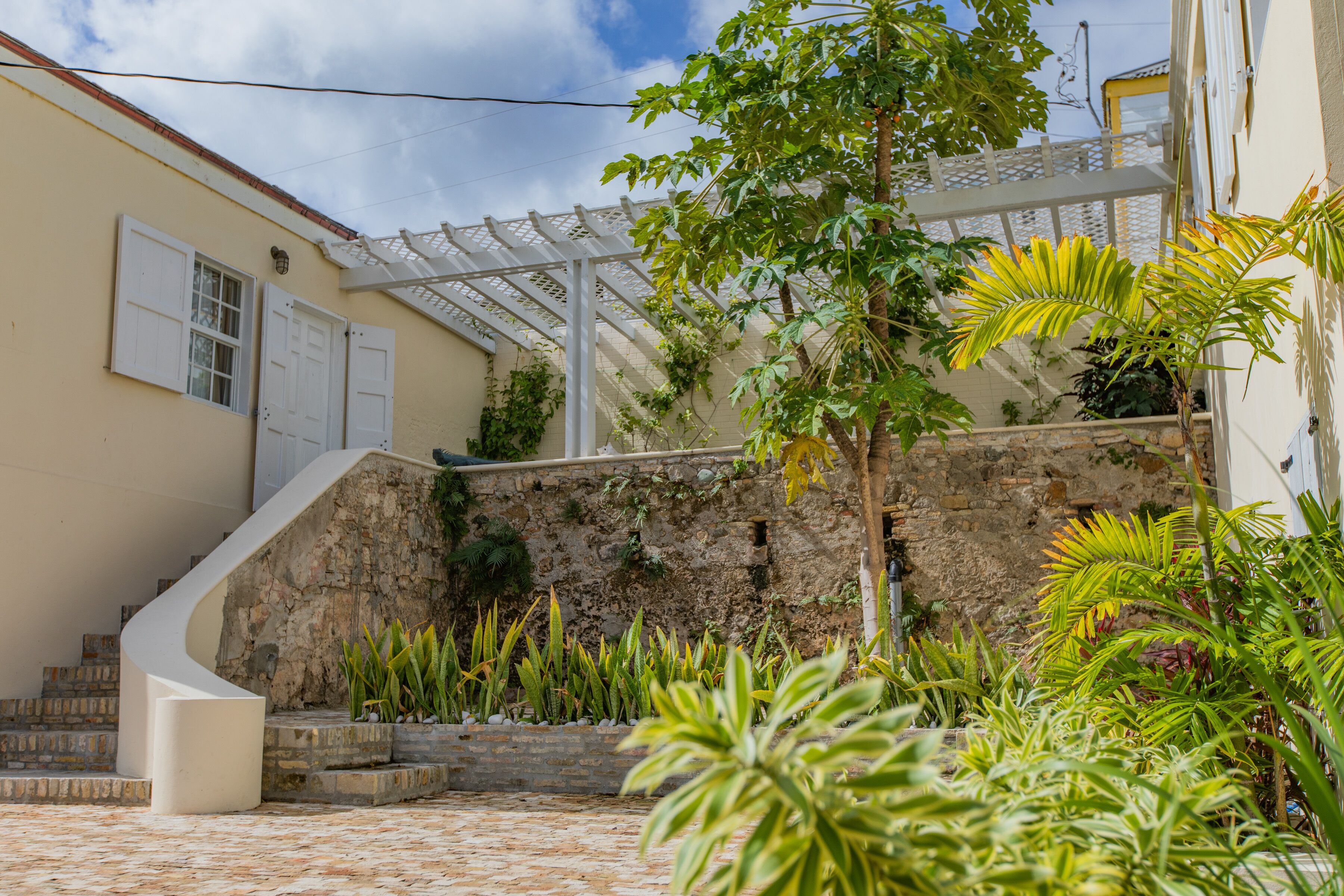 A courtyard with a stone wall, a white staircase, and various plants.