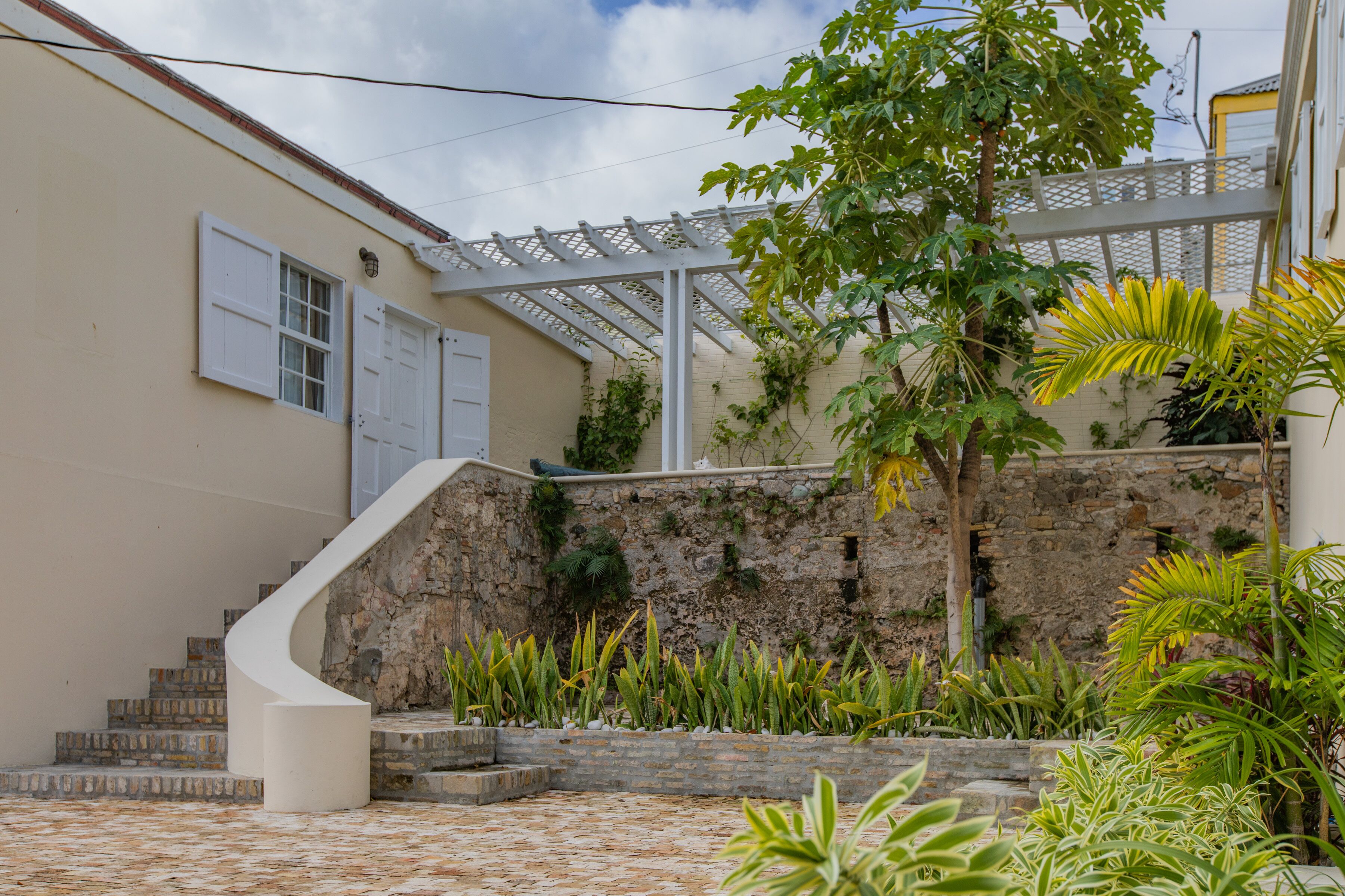 A courtyard with a stone wall, a white staircase, and various plants.