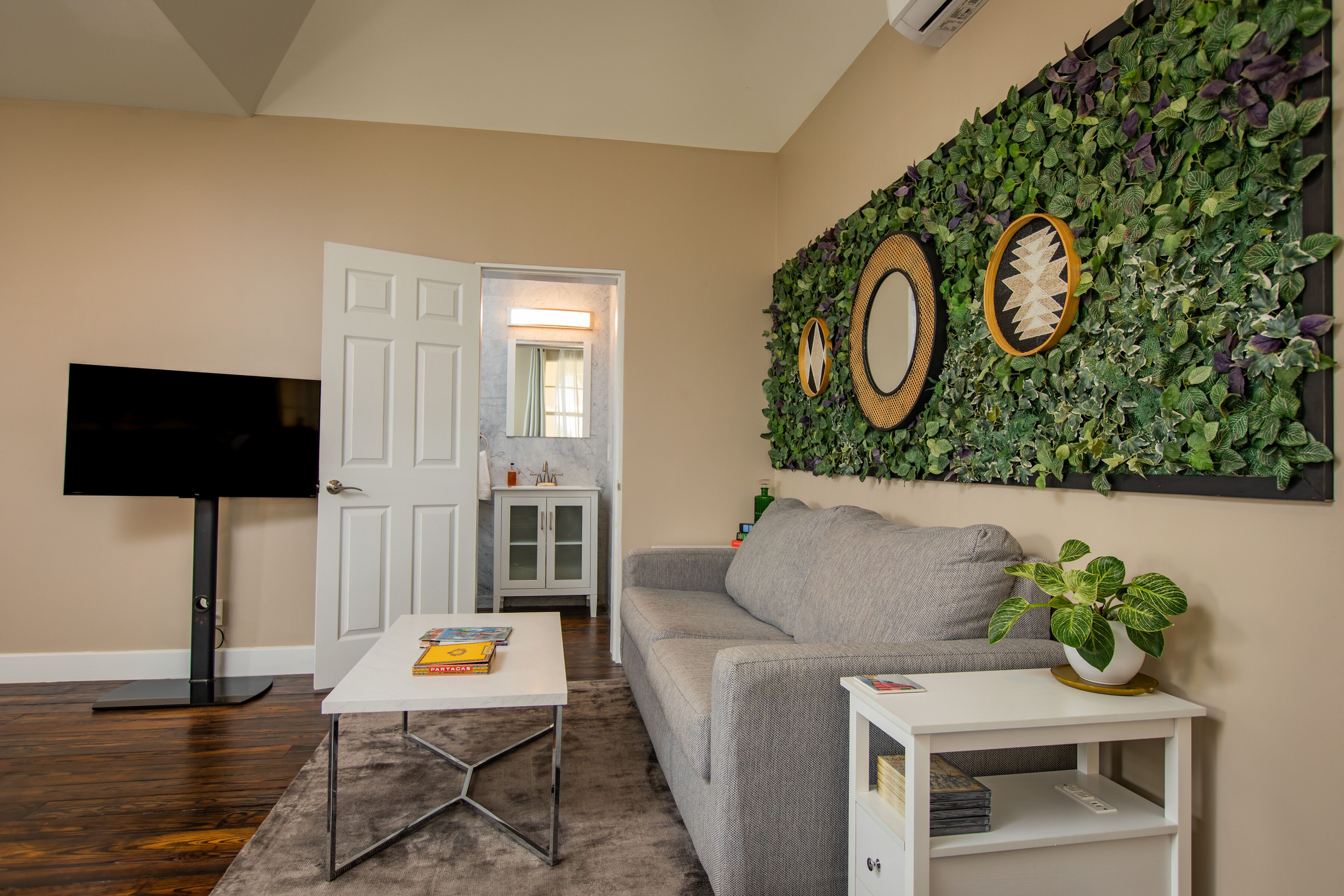 Una sala de estar con sofá, una mesa de centro, un mueble para televisión y un jardín vertical en la pared.