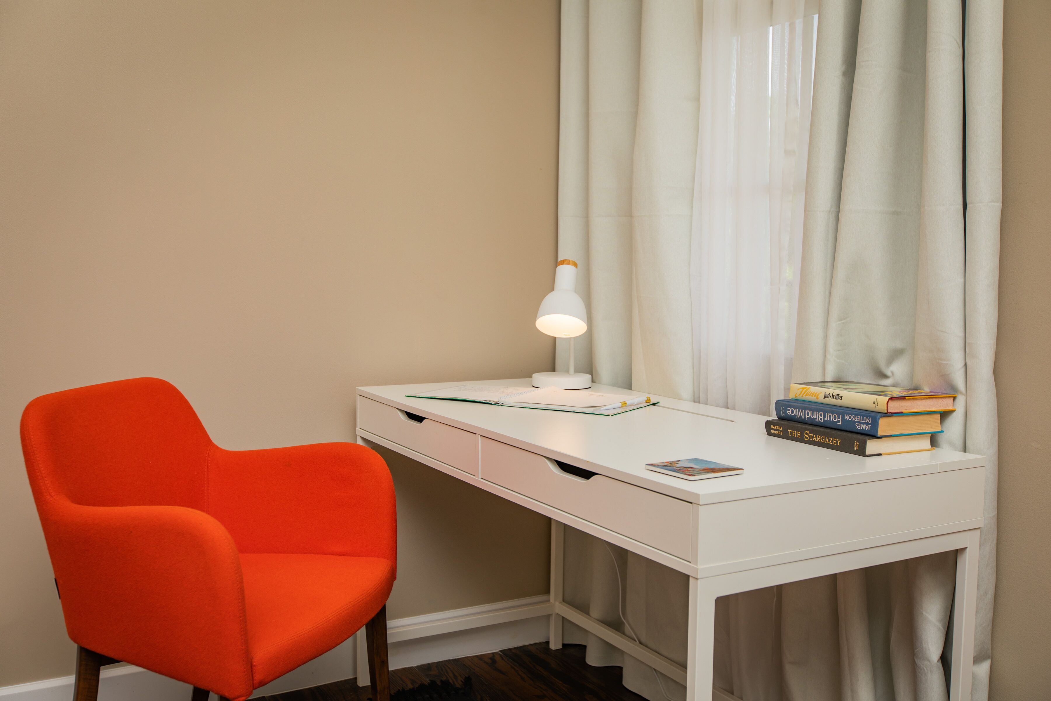 A white desk with a white lamp, a stack of books, and an orange chair.