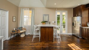 Uma cozinha com uma ilha central, banquetas brancas, uma geladeira e armários de madeira.