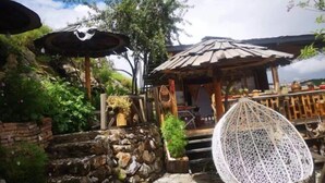 A rustic outdoor seating area with a hanging chair, stone steps, and a wooden structure with a thatched roof. - Prayer Wheel Sightseeing Inn (Shangri-La)