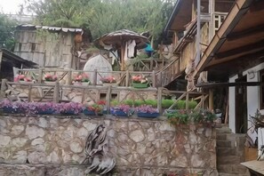 Un mur de pierres apparentes rustique, avec un escalier en bois menant à une terrasse en bois agrémentée de jardinières.