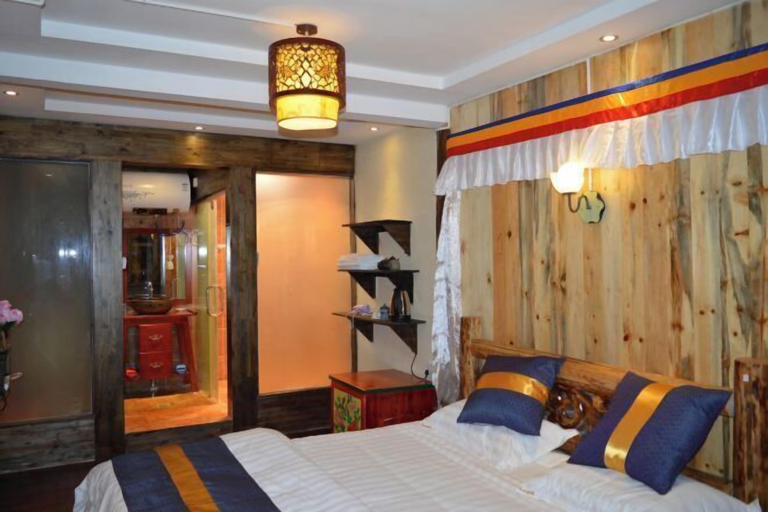 A bedroom with a wooden headboard, a bed with white bedding and blue pillows, a nightstand with a lamp, and a wooden wall paneling.
