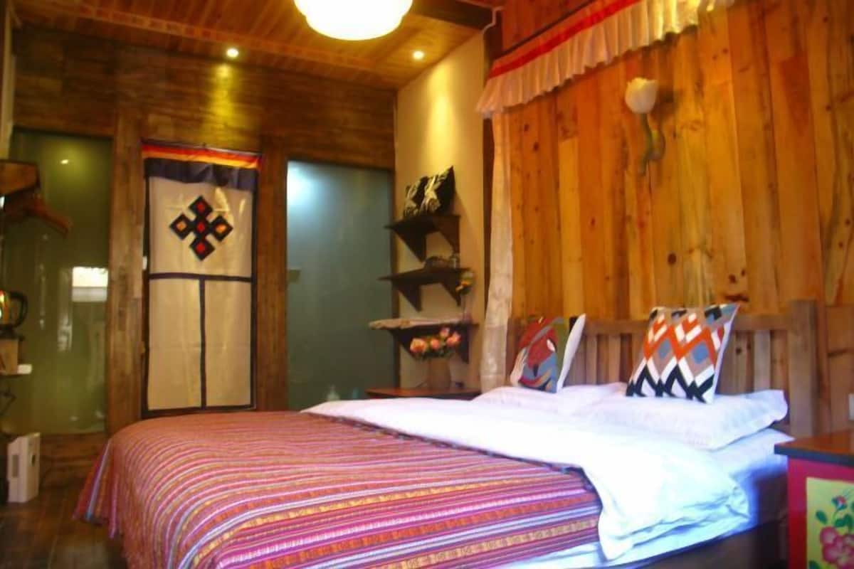 A cozy bedroom with a wooden ceiling, a bed with patterned bedding, a shelf with decorative items, and a door with a quilt.