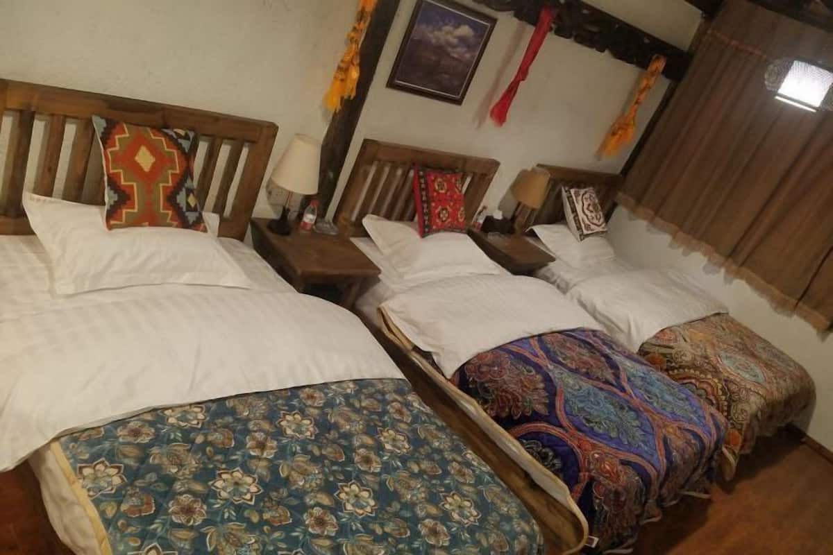 A hotel room with three beds, each with different patterned bedspreads, wooden headboards, and bedside lamps.