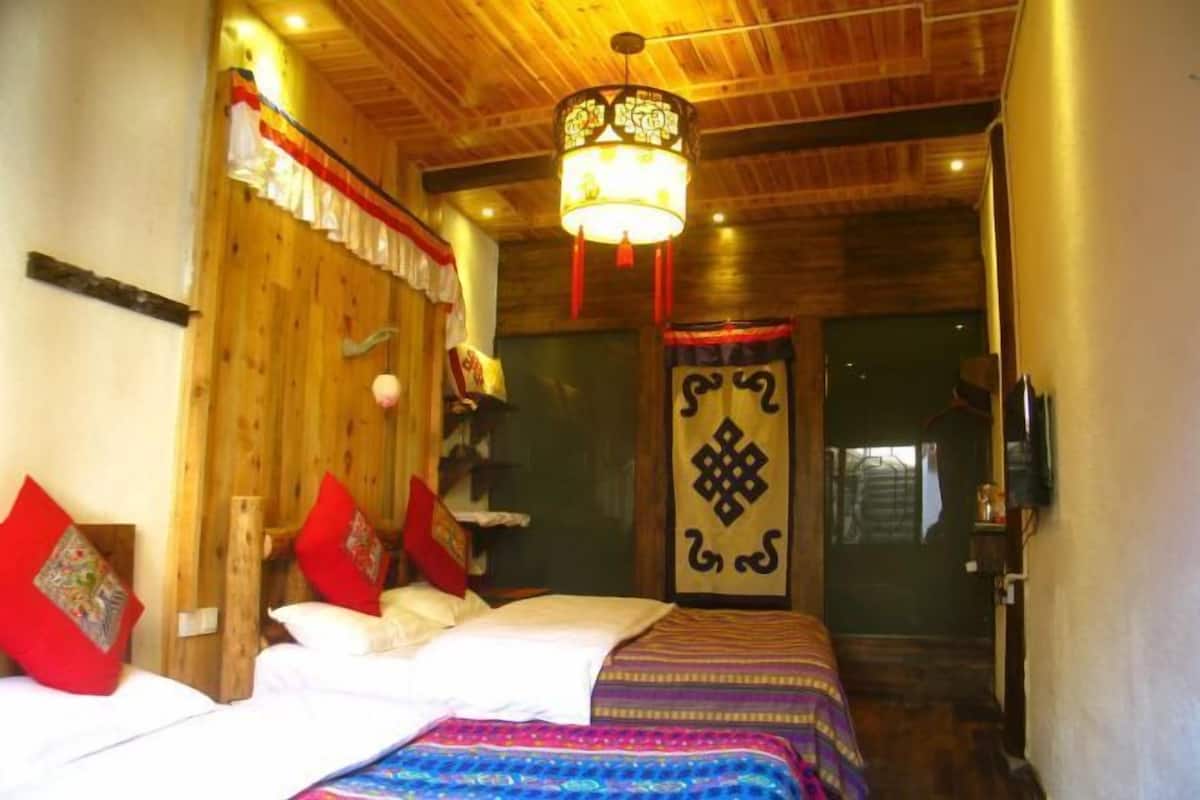 A room with a wooden ceiling, a bed with white and red bedding, a patterned bedspread, and a decorative hanging light fixture.