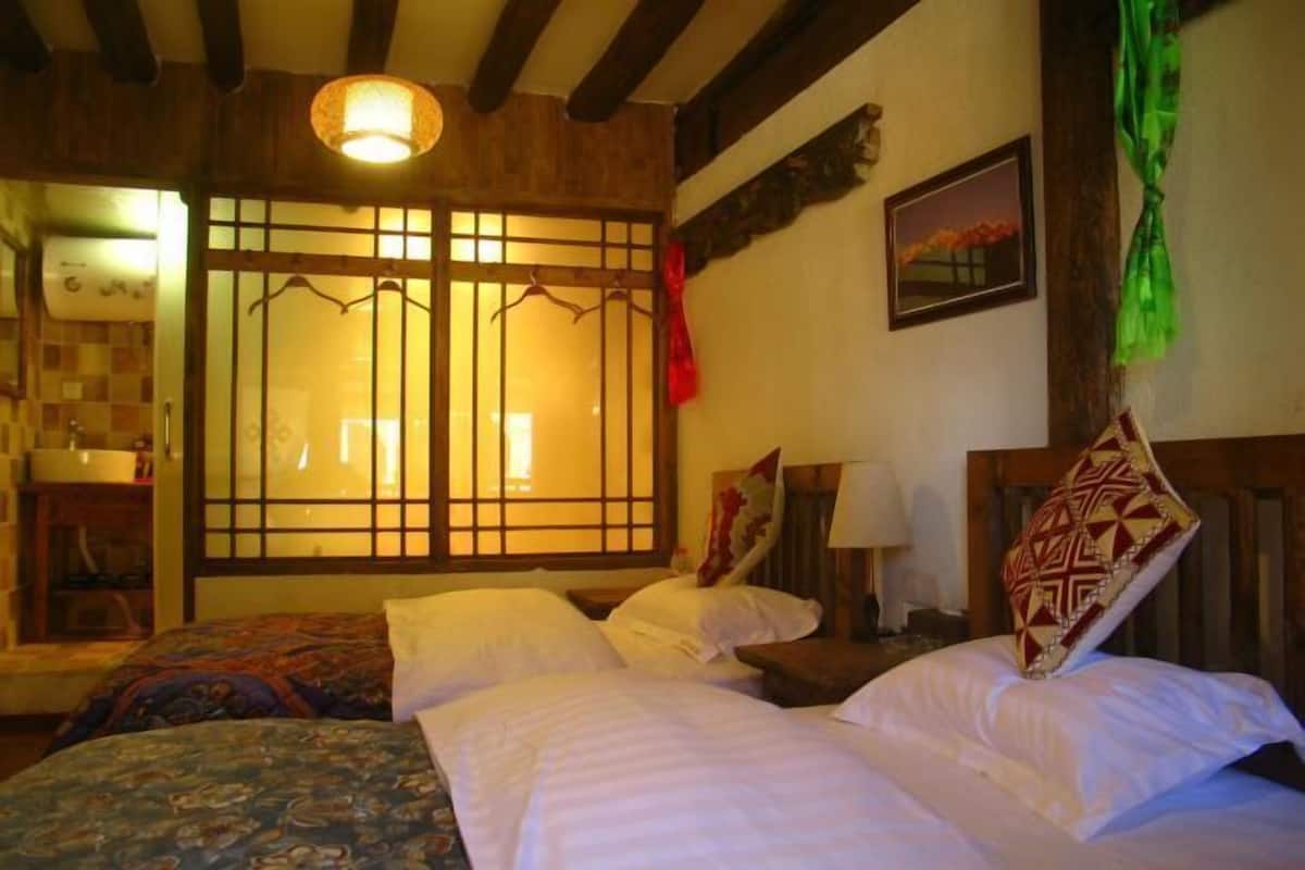 A room with two beds, a wooden ceiling, a window with a view, and a hanging decoration.
