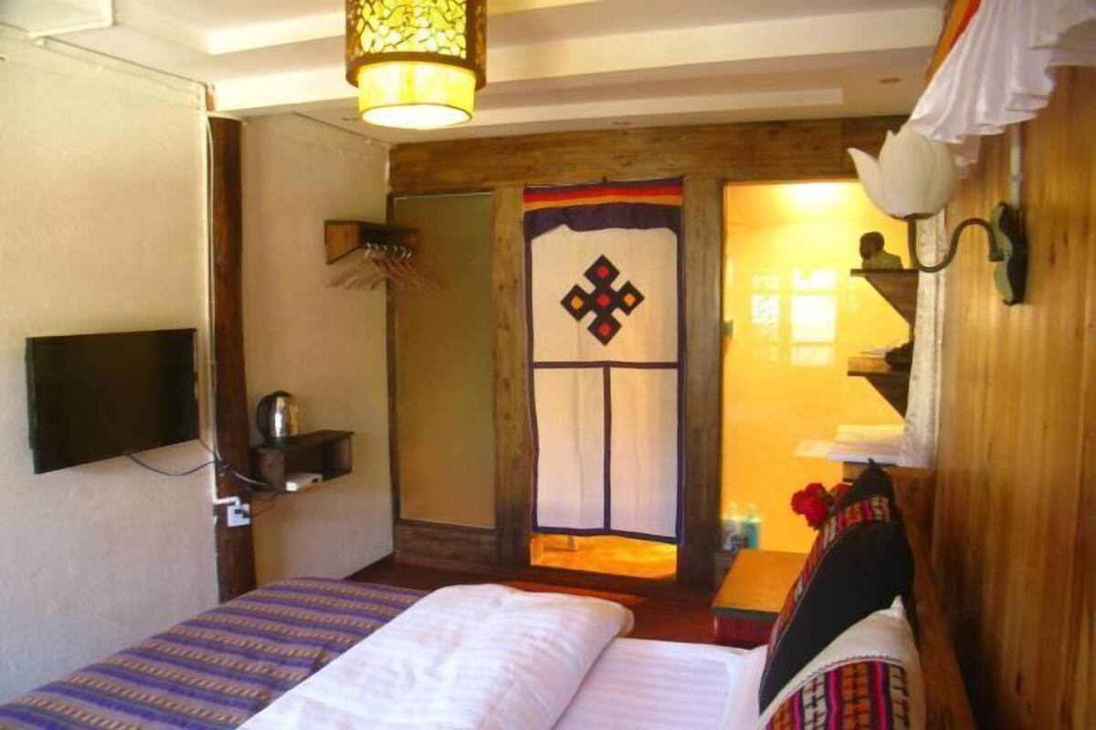 A room with a bed, a TV mounted on the wall, a wooden door with a decorative panel, and a wall-mounted light fixture.