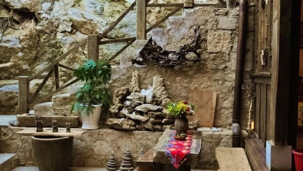 A rustic interior with stone walls, wooden benches, and a small table with a colorful cloth. - Prayer Wheel Sightseeing Inn (Shangri-La)