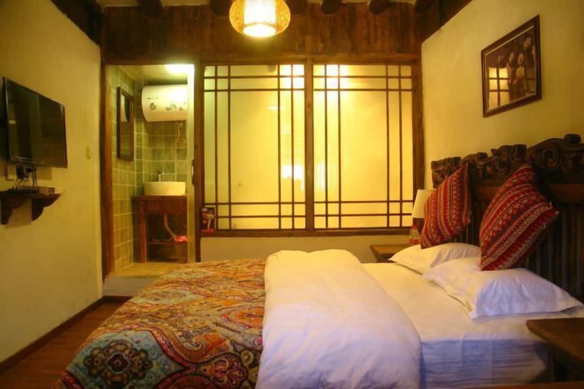 A room with a bed, a wooden headboard, a television, a bathroom with a toilet, and a window with a view.