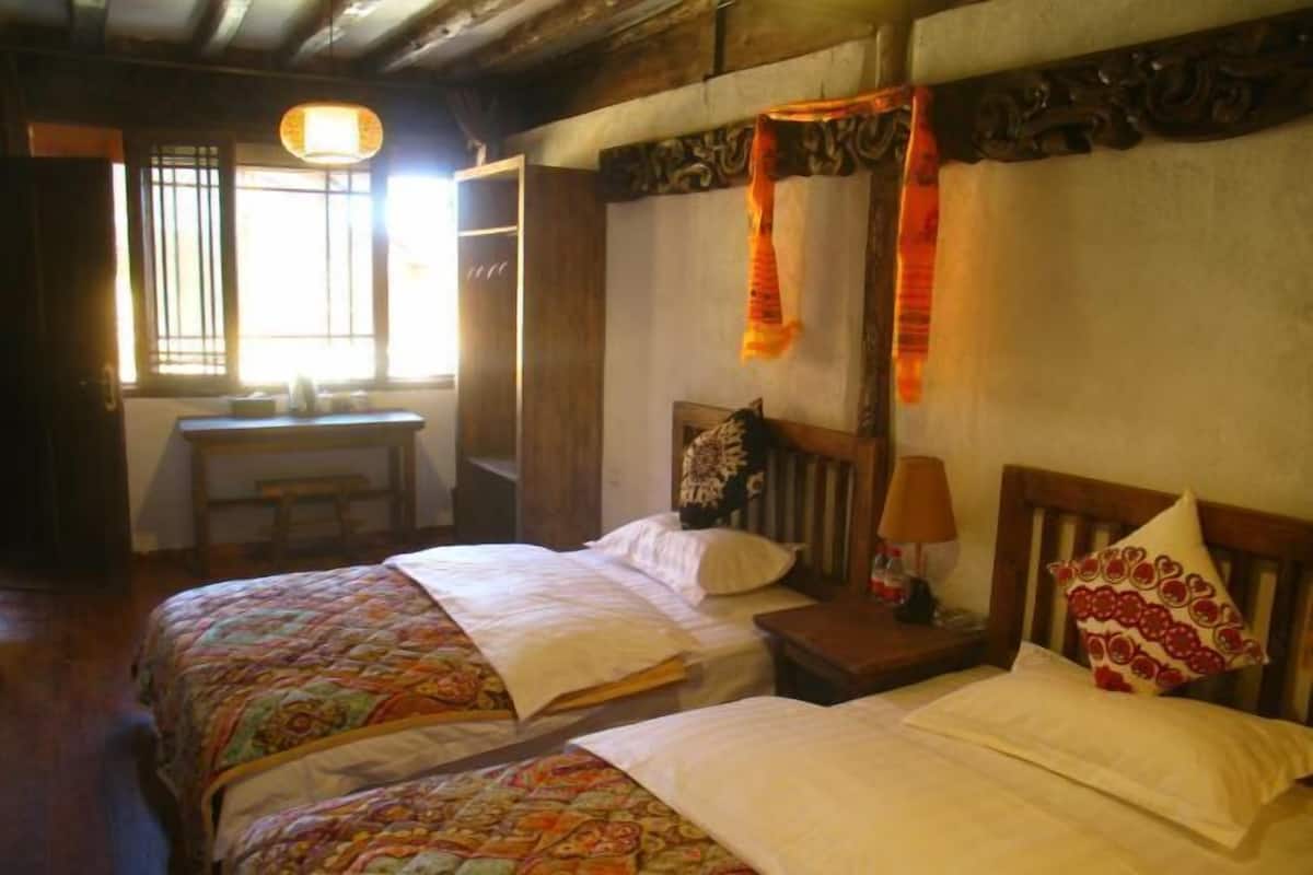 A room with two beds, a wooden desk, a chair, and a window with curtains.