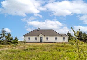 A single-story house with a gabled roof, a front door, and a small porch. - Glynsk Pier Cottage (Cashel)