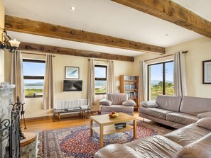 A spacious living room with a fireplace, a sofa, a coffee table, and a bookshelf. - Glynsk Pier Cottage (Cashel)