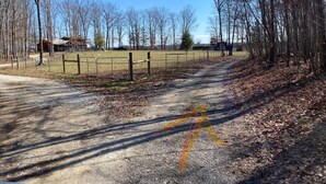 A gravel path leading through a fenced area with trees and buildings in the background. - Cabin with private pond. A peaceful escape (Deer Lodge)