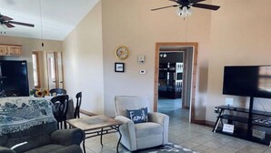 A living room with a sofa, armchair, and a TV stand. There is a dining area with a table and chairs. - Cabin with private pond. A peaceful escape (Deer Lodge)