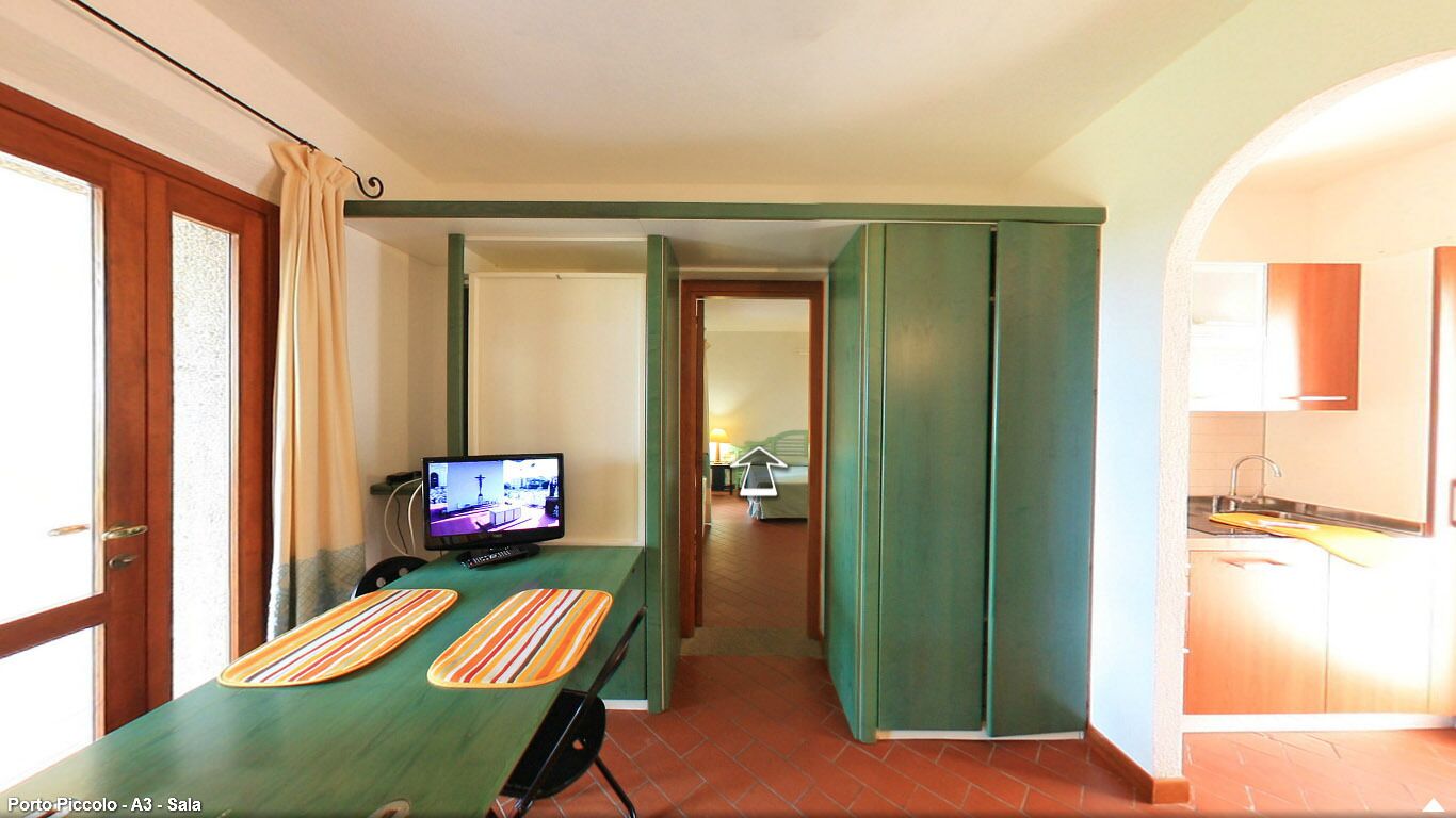 A hotel room with a bed, a television, a dining table with striped placemats, and a kitchen area.