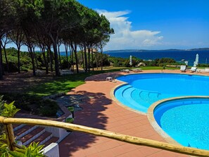 A swimming pool with a curved design, surrounded by a red-tiled deck, and overlooking a scenic view of the sea and distant hills. - Hotel Residence Porto Piccolo (Arzachena)