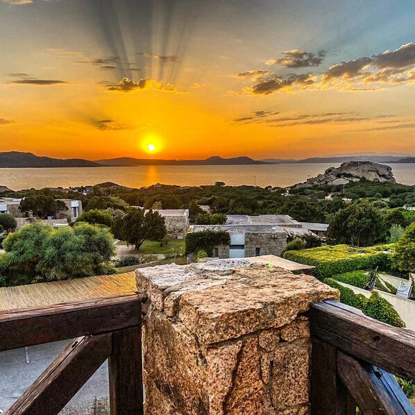 A coastal view with a sunset, stone buildings, and a prominent rock formation. - Hotel Residence Porto Piccolo (Arzachena)