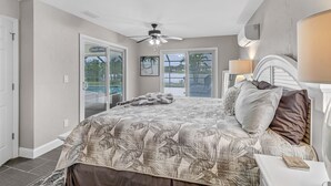 Une chambre avec un lit, une table de chevet, un ventilateur de plafond et une vue sur la piscine, visible à travers les portes-fenêtres coulissantes.