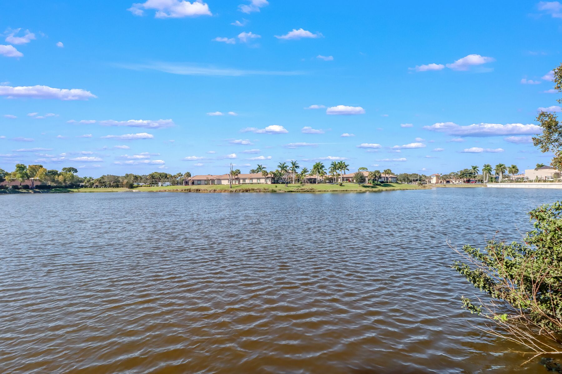 Un lago tranquilo con cielo despejado, rodeado de edificios residenciales y palmeras.