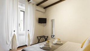 Ett hotellrum med en säng, en platt-TV som är monterad på väggen, ett fönster med gardiner och ett element.