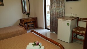 Ett hotellrum med två sängar, ett skrivbord, ett kylskåp, en stol, en TV och ett fönster med gardiner.