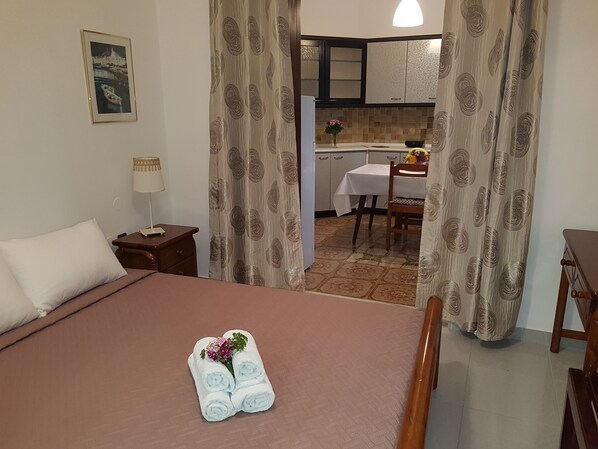 A hotel room with a bed, a nightstand, a lamp, a framed picture on the wall, and a view into the kitchen area.