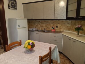 A kitchen with a refrigerator, sink, and a table with a bowl of fruit. - Georgia Old Town Apartments - Studio (N.3), Georgia Old Town Apartments Rhodes (Ρόδος,)