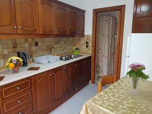 A kitchen with wooden cabinets, a sink, a kettle, and a table with a vase.