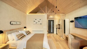 A modern bedroom with a wooden ceiling, a large bed, bedside tables, a desk, and a TV on the wall.