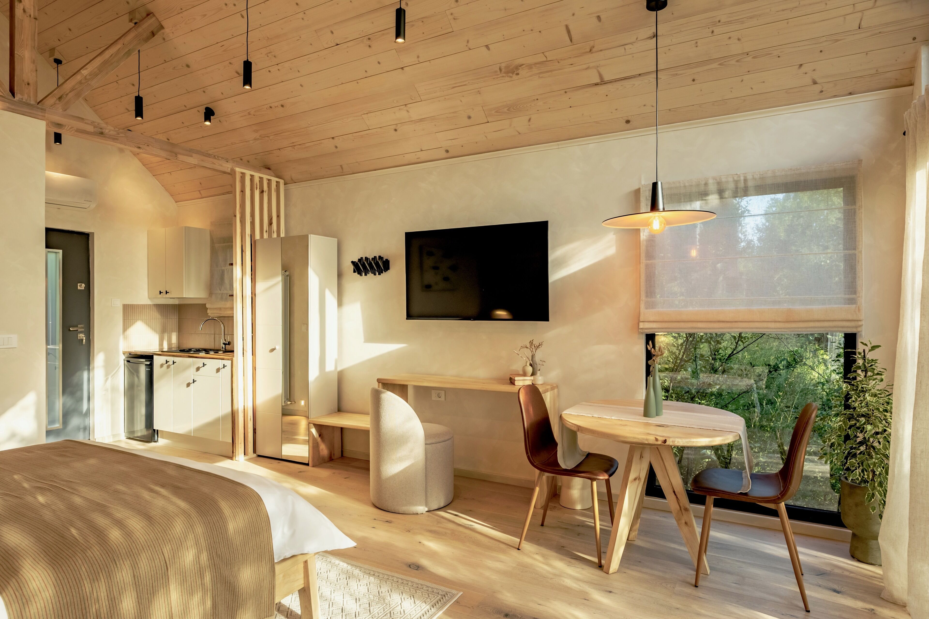 A modern, open-plan living space with a kitchen, dining area, and a large window offering a view of greenery.