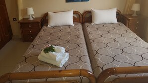 A double bed with a patterned bedspread, two pillows, a nightstand with a lamp, a painting of flowers on the wall, and a wooden headboard. - Georgia Old Town Apartments - Double Room (N.5), Georgia Old Town Apartments Rhodes (Ρόδος,)