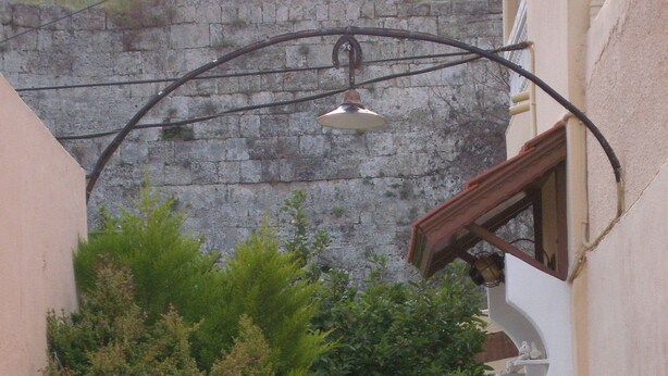 A narrow alleyway with potted plants, a hanging light fixture, and a stone wall in the background. - Georgia Old Town Apartments - Double Room (N.5), Georgia Old Town Apartments Rhodes (Ρόδος,)