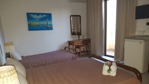 Ein Hotelzimmer mit zwei Betten, einem Schreibtisch, einem Sessel, einer Lampe, einem Bild, einem Spiegel, einem Fenster und einem Kühlschrank.