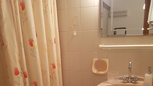 Ein Badezimmer mit Toilette, Waschbecken, einem kleinen Hocker und einer Duschvorhang mit Blumenmuster.