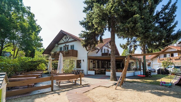 A traditional chalet with a wooden deck, outdoor seating, and a swing set. - Sommer Pension (Balatonfoldvar)