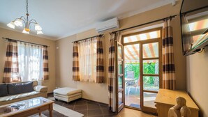 A living room with a sofa, a coffee table, a small ottoman, a wooden sculpture, and a sliding glass door leading to an outdoor area. - Sommer Pension (Balatonfoldvar)